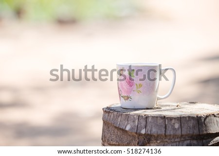 Flower cup of hot steaming coffee sitting on an old log by an outdoor.