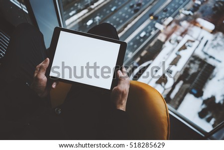 Close up mock up template of tablet pc in hands of man sitting near window of skyscraper, male arms using digital tablet with blank screen for text or logo, winter cityscape and highway outside
