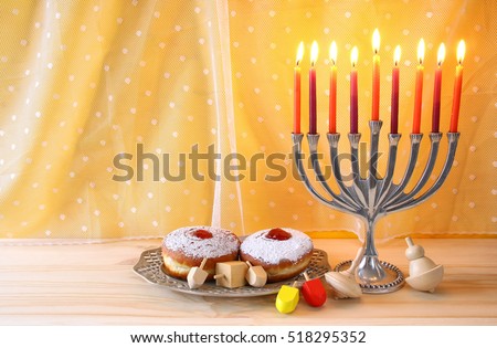 Image of jewish holiday Hanukkah with menorah (traditional Candelabra), donut and wooden dreidel (spinning top)

