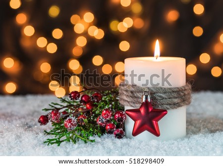 Christmas season, burning candle at snow with golden sparkling lights background 