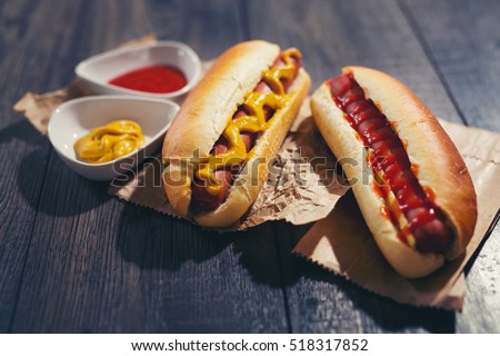 Tasty hot dogs on paper on wooden background Royalty-Free Stock Photo #518317852