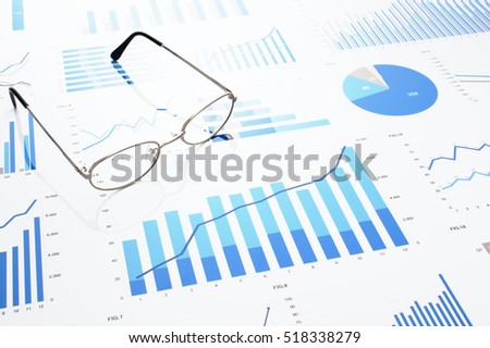 Many charts and glasses. Reviewing data. Financial reports and glasses. Reflection background.
