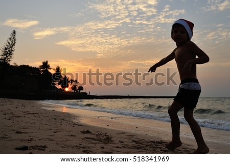 Silhouette on the beach with a beautiful background of a golden sunset: a boy dressed in shorts and a Santaâ??s cap points into the distance