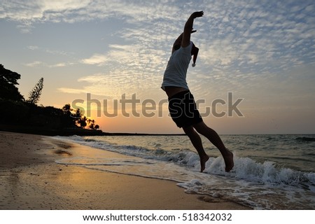 A silhouette on the beach with a background of a golden sunset: a men with Santaâ??s cap jumps high, body stretched out in an arc. Wet sand and sea water reflects the sunshine