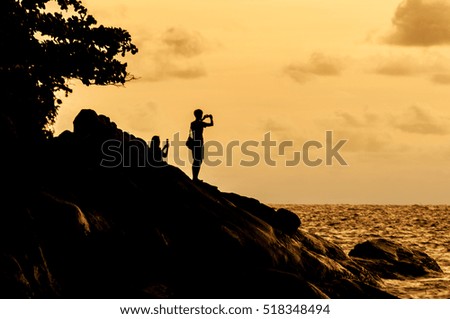 Sunset on the beach silhouette rock, trees and tourists take picture 