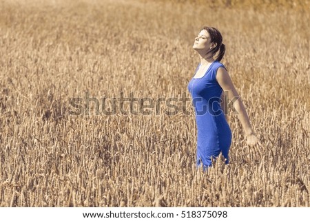 Beautiful young woman with pretty dress in nature. Beauty girl in cornfield in autumn. The blue of the dress is the only blue in the picture. Perfect for coloration