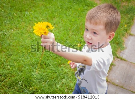 Little Caucasian 3 year old boy handing yellow dandelion flowers to somebody. Sincerity sharing stock image.