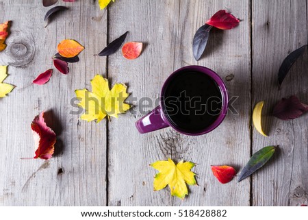 Cup of coffee surounded by red, purple and yellow fall leaves