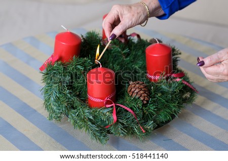Woman lighting festive red advent candles on a traditional homemade evergreen pine Christmas wreath with cones, close up view