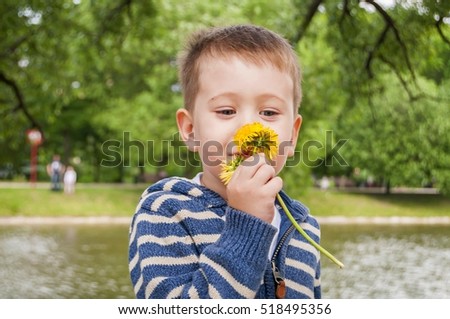 Little Caucasian 3 year old boy smelling yellow dandelion flower in the park.