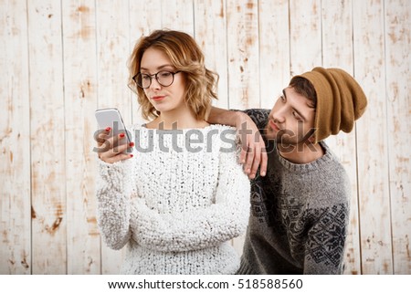 Man unnerve his girlfriend looking at phone over wooden background. Royalty-Free Stock Photo #518588560