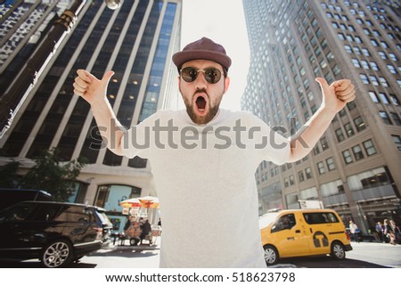 Happy funny bearded man laughing and showing thumbs up in Manhattan. Hipster tourist posing for photo while travel in New York.
