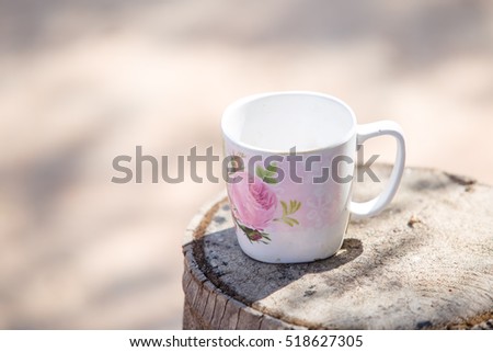 Flower cup of hot steaming coffee sitting on an old log by an outdoor.