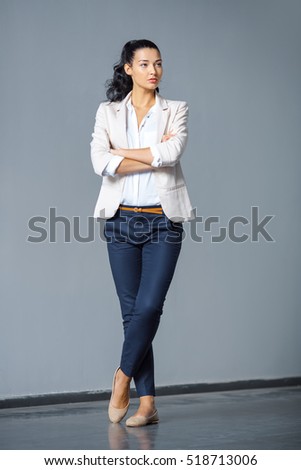 Beautiful brunette business woman in suit standing outdoors against gray background and looking away in full lenght. Copy space
