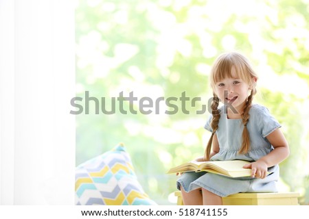 Cute little girl with book sitting on yellow stool