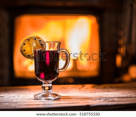 Hot mulled wine with orange slice, cloves and cinnamon stick. Fireplace with warm fire on the background.