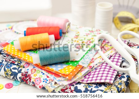 sewing, sewing on the sewing machine, sewing supplies, colored sewing threads, colored pieces of cloth, needles, centimeter, tailors scissors on white wooden background Royalty-Free Stock Photo #518756416