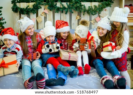 Group of kids in red hat lying on the bed next to the Christmas tree holding gifts and smiling