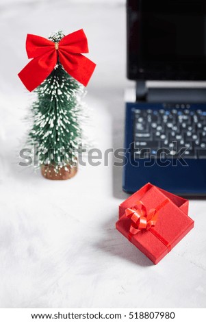 Laptop, little christmas tree and red gift box on concrete background