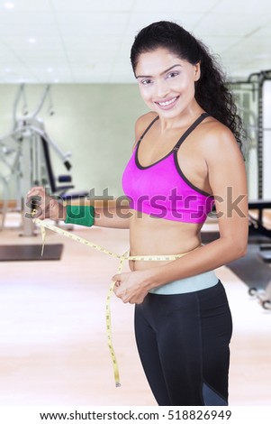 Picture of sporty woman measures waist with measuring tape while smiling at the camera