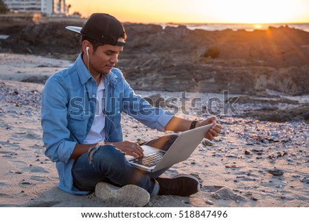 Young african coloured man working on laptop at the beach, Cape Town, South Africa Royalty-Free Stock Photo #518847496