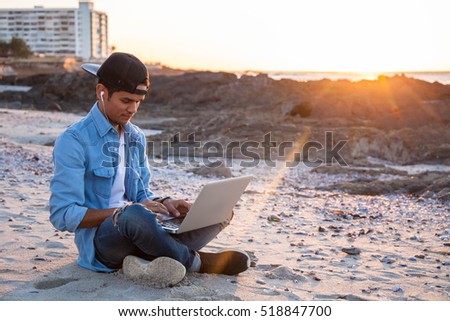 Young african coloured man working on laptop at the beach, Cape Town, South Africa Royalty-Free Stock Photo #518847700