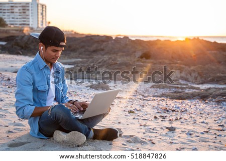 Young african coloured man working on laptop at the beach, Cape Town, South Africa Royalty-Free Stock Photo #518847826