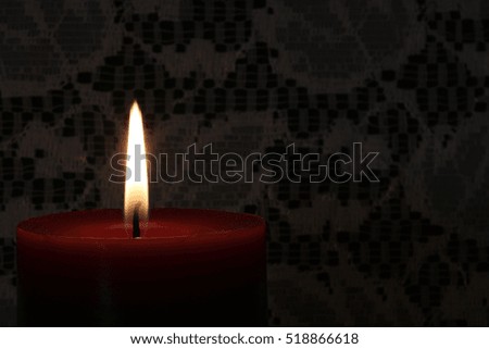 Red Candle with Flame Against White Lace over Green Background - close up photograph of a red candle with a flame against a lace background. Space for text on right side. Selective focus on candle.