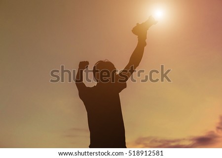 Silhouette of a young man like to travel and photography, extend the arms the sunset ,sunrise. with holding camera