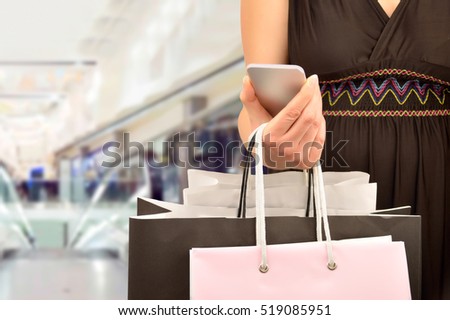 Cropped shot of shopper woman holding the shopping bags an using the smart phone at the center mall. Concept of shopaholic woman.