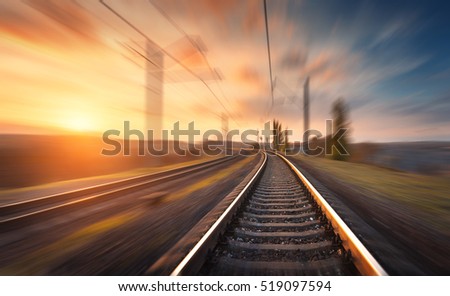 Railroad in motion at sunset. Railway station with motion blur effect against colorful blue sky, Industrial concept background. Railroad travel, railway tourism. Blurred railway. Transportation Royalty-Free Stock Photo #519097594