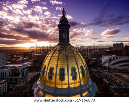 Aerial/Drone photograph of a sunset over the golden Colorado state capital building.  Capital city of Denver.  The Rocky Mountains can be seen on the horizon