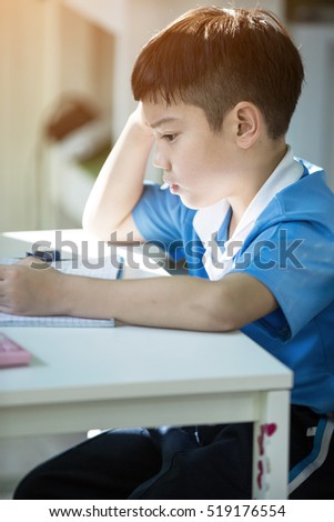 Young asian boy doing his homework and thinking 