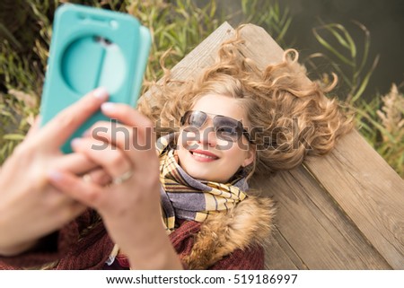 Smiling woman in sunglasses lying on the pier making a selfie