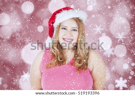Portrait of beautiful fat woman wearing santa hat and smiling at the camera with christmas background