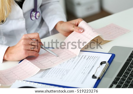 Doctor hands with cardiogram chart on clipboard pad fill medical history with silver pen. Cardio therapeutist assistance, physician make cardiac physical, pulse measure document, arrhythmia idea Royalty-Free Stock Photo #519223276