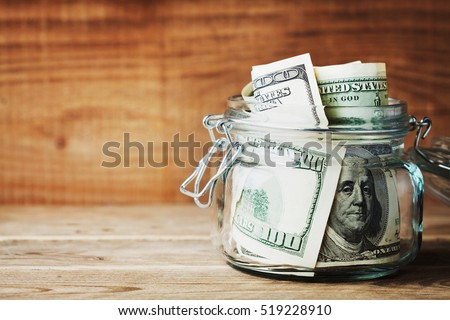 Dollar bills in glass jar on wooden background. Saving money concept Royalty-Free Stock Photo #519228910
