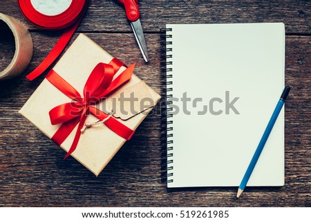 View above brown gift box and notebook with tag on wood background with space.