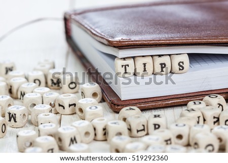 Word Tips written on a wooden block in a book. On old white wooden table.