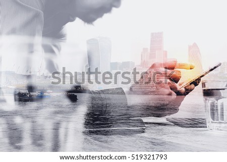 Double exposure of businessman hand using mobile payments online shopping,omni channel,laptop computer on wooden desk,London architecture buildings 