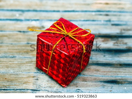Red wrapped gift on wood background. Christmas gift box in foliage wrapping with gold thread bow. New Year fir tree ornament closeup on rustic backdrop. Winter holiday symbol. Christmas season banner