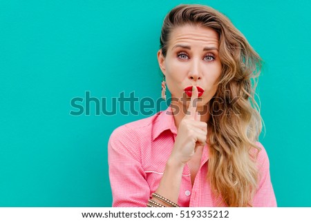 Keep secret! Pretty young woman showing silence sign with her finger on lips. Colorful portrait with green background.