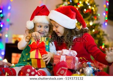 two little girls are opening presents around the Christmas tree