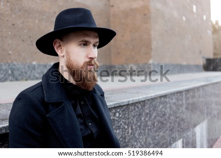 A young stylish bearded hipster in a hat and coat on the street. man enjoying city 