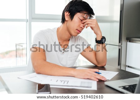 Tired asian man by the table with docements and laptop