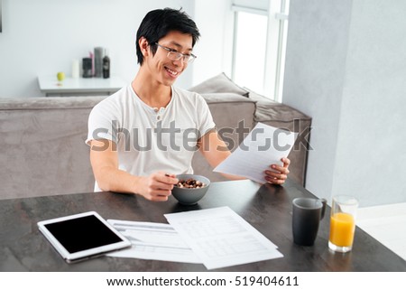 Smiling asian man working and eating by the table.