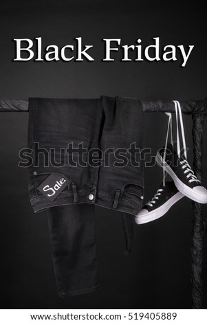  Black friday. Sale sign. Black and white sneakers and pant, jeans hanging on clothes rack on black background.  Close up. 