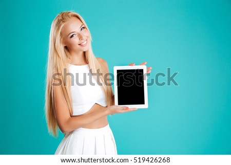 Portrait of a happy blonde woman standing and showing blank screen tablet isolated on the blue background