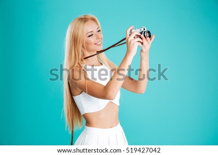 Portrait of a beautiful smiling woman taking picture with retro camera and looking away isolated on the blue background