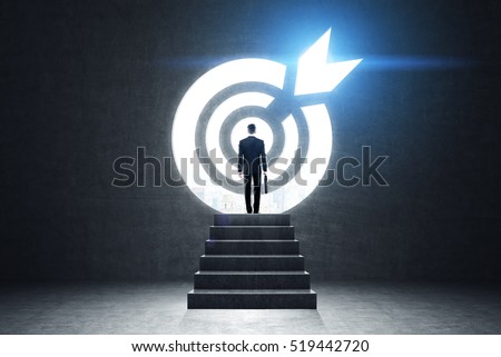 Rear view of a businessman with a suitcase standing near target sketch on black wall. Concept of achieving your goal. Toned image Royalty-Free Stock Photo #519442720